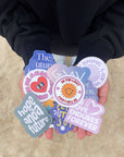 Hands holding colorful Christian stickers with encouraging messages from Elevated Faith