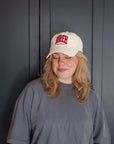 Woman wearing a Jireh embroidered hat with a grey shirt against a dark paneled wall