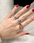 Hand with red nail polish wearing multiple rings on a neutral background