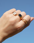 Hand wearing three gold rings against a clear blue sky