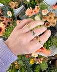 Hand wearing the Cross Gemstone Gold-Tone Ring with other rings beside colorful flowers