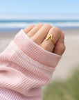 Wavy Cross Gold-Tone Ring worn on a hand extending from a pink sleeve with the beach in the background