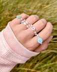Hand wearing multiple beaded rings with a blurred grass background