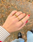 Hand with red nails wearing the Stacked Cross Gem Gold-Tone Ring alongside other rings outdoors