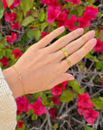 Close view of the Eden gold-tone ring worn on a hand against pink flowers