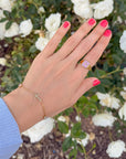 Everlight cross bracelet worn with rings and pink nails above white flowers