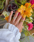 Bloom Again Enamel Ring worn on a hand beside a colorful bouquet and other gold-tone rings