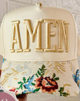 Cap with 'AMEN' embroidery and floral design, held against a light background
