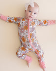 Baby in a floral onesie with pink accents on a beige background