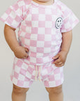 Child wearing a pink and white checkered outfit with a smiley face design on a plain background