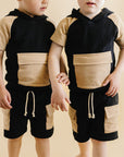 Two young boys wearing matching black and beige outfits on a beige background