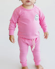 Baby wearing a pink outfit with smiley face design on a white background