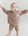 Child wearing a brown sweatshirt with a smiley face design on a plain background