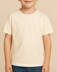 Young boy wearing a natural-colored Rabbit Skins 3321 Youth T-Shirt on a neutral beige studio background — soft ringspun cotton blank ideal for custom printing by Lumiere Vive.