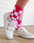 White sneakers with red and white checkered socks on a wooden floor.