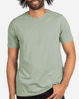 Male model wearing a sage green Next Level 3600 Unisex Cotton T-Shirt on a light background — premium ringspun cotton blank ideal for custom printing by Lumiere Vive.