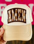 Beige cap with 'Amen' patch held by a hand against a pink background with text.