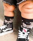 Child wearing black and white Vans shoes with socks, standing on a carpeted floor.