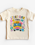 Children's t-shirt with 'First Day Vibes' design featuring a school bus and colorful elements on a white background.