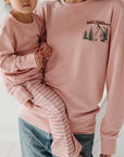 Woman holding a child both wearing pink sweatshirts with nature-themed designs.