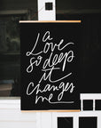 A Love So Deep Christian wall art hanging from a wood banner hanger in front of a window