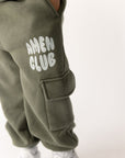 Close-up of white Amen Club lettering and cargo pocket on hunter green kids sweatpants