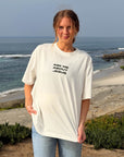 Model wearing cream Ask Me About Jesus graphic tee by the coast