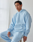Person wearing a light blue tracksuit sitting on a wooden stool in a minimalistic room.