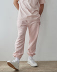 Man wearing a pink outfit with white sneakers against a plain background