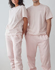 Two people wearing matching light pink outfits standing against a white wall.