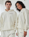 Two people wearing matching cream-colored hoodies and pants with a brand logo.