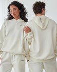 Two people wearing matching cream-colored tracksuits in a minimalistic setting.