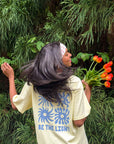 Model holding tulips while wearing the Morning Sun Be the Light tee with blue sun and floral graphics on the back