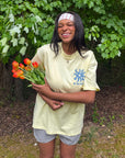 Model holding orange tulips while wearing the yellow Be the Light Unisex Tee with white shorts