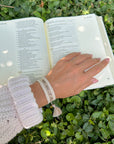 Taupe WWJD bracelet worn on a wrist beside an open Bible outdoors