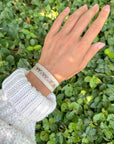 Close-up of the beige WWJD woven bracelet worn against green foliage