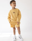 Child wearing the New Wheat yellow Better Days Butterfly crewneck sweatshirt with coordinating shorts.