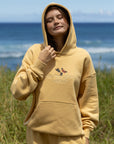 Person wearing a yellow hoodie and shorts with a graphic design, standing in a grassy area with ocean in the background