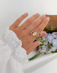 Bloom Again Enamel Ring worn on a hand beside a pastel floral arrangement