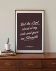 But the Lord Stood Scripture wall art with light script on a deep brown background, displayed in a frame above a wooden dresser