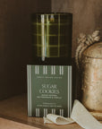 Sugar Cookies soy candle in an olive glass jar displayed above its coordinating green gift box.
