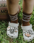 White Crocs with sports-themed designs on grass next to a Wilson NCAA football.