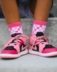 Pink and black sneakers with checkered socks worn by a person.