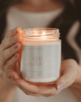 Hands holding a lit Cashmere and Vanilla candle in a clear jar with a striped label