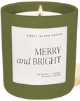 Merry and Bright soy candle in a matte olive glass jar with a cream label and wooden lid beside it.