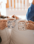Two people holding floral gold handle mugs, including the blue Best Mom Ever design