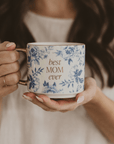 Person holding a blue floral Best Mom Ever mug with gold lettering and handle