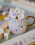 Mahjong gold handle mug filled with game tiles beside a mahjong tile rack