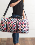 Person holding a checkered duffel bag with smiley face patterns against a white wall.