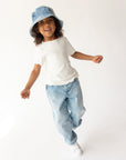 Child wearing a white t-shirt, blue jeans, and denim bucket hat on a white background
